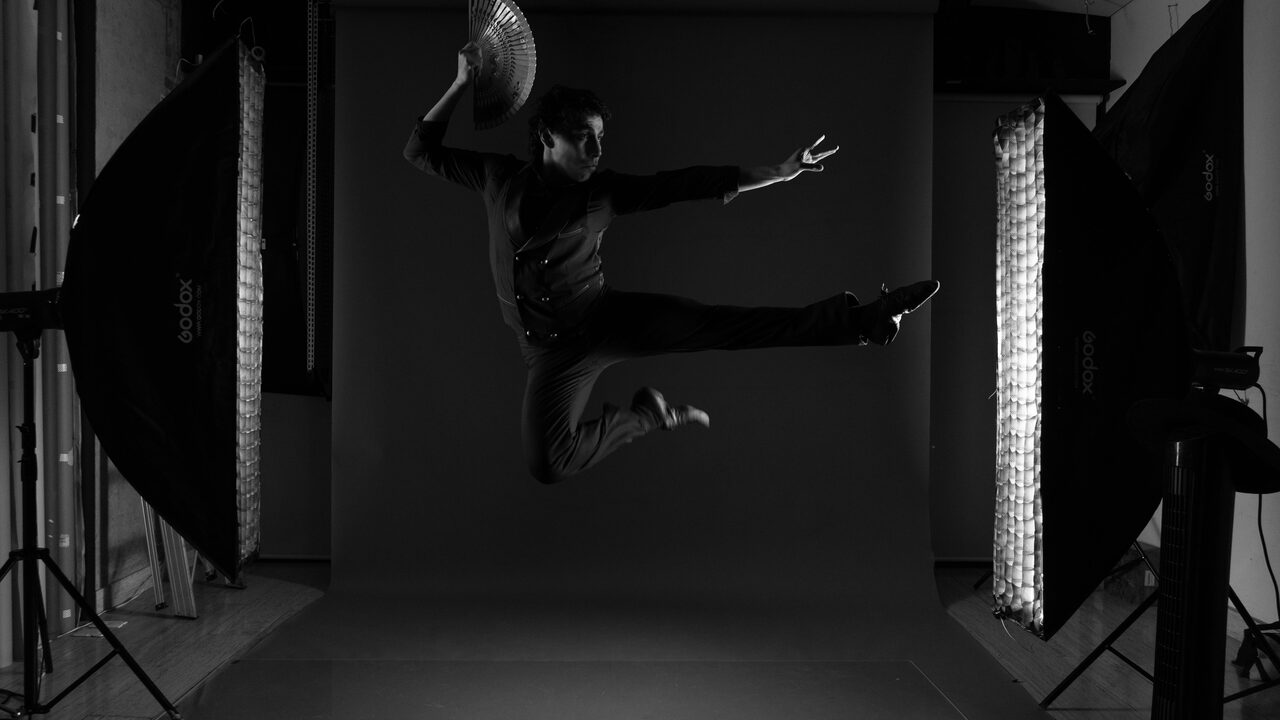 Dancer mid-leap in dark mocap studio wearing suit with glowing reflective markers — movement fingerprint capture